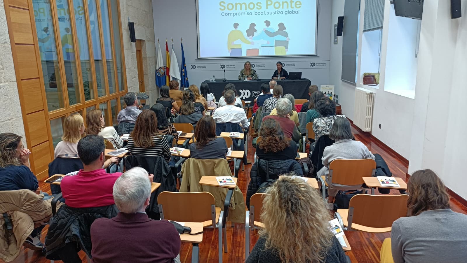 Somos Ponte. Paula Bouzós e María Paz Salón de actos do Edificio Administrativo da Deputación de Ponrevedra cheo de persoas para escoitar a conversa "Cando a cooperación sanda". Na mesa, a deputada de Benestar Social, Paula Bouzós, e a presidenta da Coordinadora Galega de ONGD, María Paz